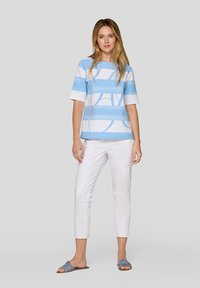 Blue and white striped short-sleeve top with abstract pattern, paired with white cropped pants and blue slide sandals. Smooth fabric texture.