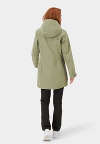 Snygg, knälång olivgrön jacka med huva, svarta detaljer och en slät textur, ihopparad med mörka byxor och vita skor.
