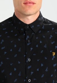 Camicia nera con bottoni, caratterizzata da un design a righe blu. Presenta un colletto standard e un piccolo logo giallo sul petto.
