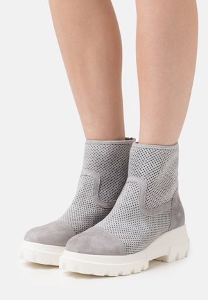 Bottes chevilles en suède gris avec côtés perforés, bout arrondi et semelles épaisses en caoutchouc blanc. Comprend des accents lisses et un design sans lacets.