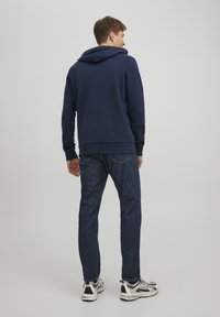Navy hooded sweatshirt with ribbed cuffs, paired with dark denim jeans. The outfit is completed with black and white athletic shoes.