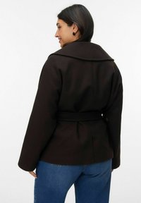 Chaqueta marrón con cinturón y cuello con muesca, hecha de tela suave. La parte posterior tiene un ligero vuelo en la cintura y cuenta con mangas largas.