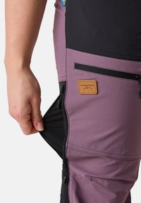 Pantaloni da esterno Swedemount in viola e nero con tasca laterale con zip e tessuto texture. Presentano una toppa con logo e cuciture a contrasto.