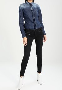 Jeansskjorta i mörkblå med volangdetalj fram och långa ärmar. Matchad med svarta skinny jeans och vita ankelstövlar.