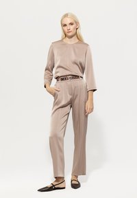 Beige satin blouse with three-quarter sleeves, paired with matching high-waisted trousers. Features a decorative belt and pointy flats.