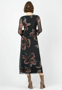 Schwarzes Kleid mit floralen Mustern in Pink- und Teal-Tönen, aus transparenter Material gefertigt, mit langen Ärmeln und einem fließenden Design bis zur Knöchellänge, kombiniert mit beigen Stiefeln.