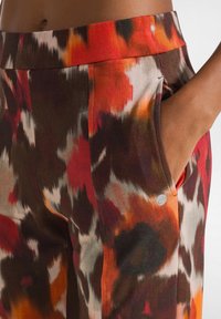 Elastische tailleband broek in een multicolore abstracte print met tinten oranje, rood en bruin; heeft zijzakken en een zachte stofstructuur.