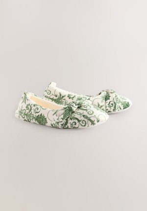 White fabric shoes with green floral and scroll patterns. Soft texture, flat sole, and a bow accent on the front. Rounded toe design.