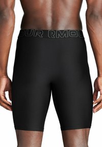 Shorts compressivi neri con una superficie liscia, dotati di una ampia vita elastica con il logo "UNDER ARMOUR" in lettere nere a contrasto.