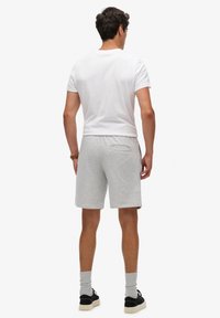 Pantalones cortos de algodón grises con una cintura elástica y un bolsillo trasero, combinados con una camiseta básica de cuello redondo blanca y zapatillas negras.