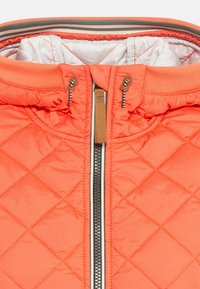 Gequilted pufferjack in helder koraal. Beschikt over een staande kraag, een zilveren rits en contrasterende binnenvoering. Gemaakt van nylonstof.