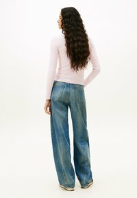 Top de manga larga rosa claro combinado con unos vaqueros holgados de denim azul. Los vaqueros tienen un lavado desgastado y bolsillos traseros tradicionales.