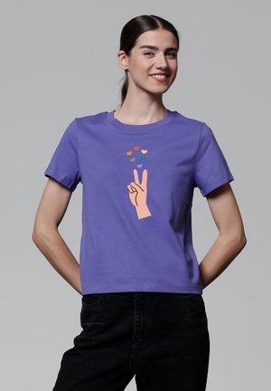 Lila Kurzarm-T-Shirt mit einem Grafikdesign einer Hand, die ein Peace-Zeichen macht, darüber bunte Herzen. Hergestellt aus glattem Baumwollmaterial.