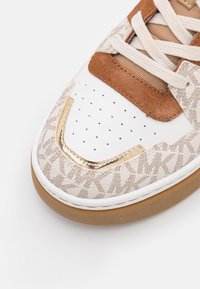 Sneaker con una punta in pelle bianca con fori, accenti in suede marrone, un motivo testurizzato e un dettaglio metallico dorato sul lato.