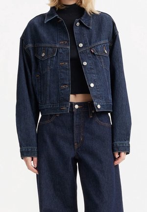 Kvinde iført mørkeblå cropped denimjakke over sort ribbet crop top og matchende højtaljede viddebukser i jeans.