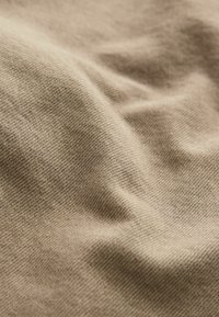 Tissu en coton beige, arborant une texture douce avec des motifs de tissage visibles et de légères rides, créant une apparence détendue.