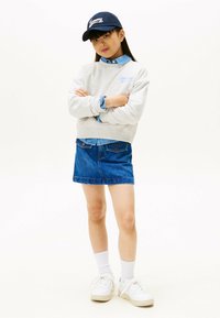 Sudadera gris con el logo "Tommy", camisa de chambray de mezclilla, falda de mezclilla azul, zapatillas blancas y gorra de béisbol azul marino. Tejidos texturizados, estilo casual.