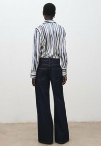 Majica z dolgimi rokavi z belimi in mornarsko modrimi črtami z ovratnikom; kombinirana s širokimi kavbojkami temno modre barve z zadnjimi žepi in všitimi detajli.