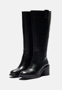 Stivali neri in pelle al ginocchio con tacco a blocco, texture liscia e cuciture a contrasto. Presentano un linguetta superiore per indossarli facilmente.