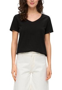 Zwarte katoenen t-shirt met korte mouwen en een V-hals, gemaakt van een zachte stof, gecombineerd met losse witte broeken.
