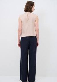 Blusa beige senza maniche con dettaglio a buco di serratura sulla schiena, abbinata a pantaloni ampi blu navy. Tessuto morbido, design minimale, linee pulite.