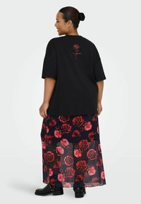 Zwarte oversized T-shirt met een rode rozenafbeelding op de achterkant, gecombineerd met een doorschijnende maxi-jurk met een bloemenprint in rood en donkerblauw.
