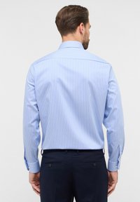 Camicia a maniche lunghe a righe blu chiaro, con polsini abbottonati e colletto stretto. Realizzata in un tessuto liscio e traspirante.