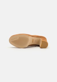 Stivaletto marrone in suede con suola beige liscia. Presenta un logo sottile sulla suola e un motivo testurizzato lungo la parte inferiore per una migliore aderenza.