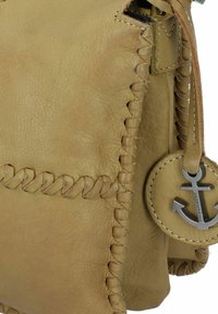 Borsa in pelle gialla con cuciture intricate e un ciondolo a forma di ancora. Presenta una texture morbida e una forma rettangolare compatta.