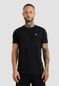 Schwarzes Baumwoll-T-Shirt mit Rundhalsausschnitt und kurzen Ärmeln. Auf der linken Brust befindet sich ein kleines weißes Grafikmotiv mit gekreuzten Messern. Geschmeidige Textur.