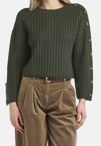 Zielony sweter z prążkowanego dzianiny z okrągłym dekoltem i guzikami na rękawach. Połączony z brązowymi spodniami sztruksowymi z zakładkami.