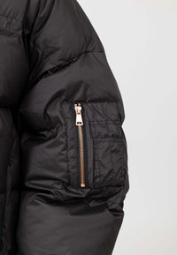 Giacca a giacca nera con sezione trapuntata, tasca con zip e hardware dorato, e polsini elasticizzati per una vestibilità aderente.