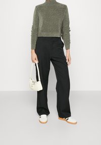 Dzianinowy, oliwkowozielony sweter golf z dopasowaną talią; czarne spodnie o szerokich nogawkach; biała torebka; białe trampki z czarnymi paskami.