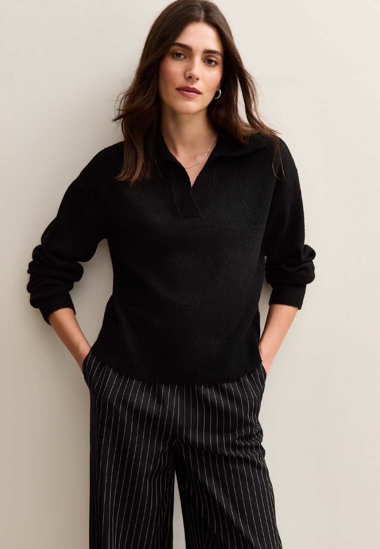 Czarny sweter w dzianinę z kołnierzykiem, luźny krój i ściągacze u rękawów. Połączony z czarno-białymi spodniami w paski o szerokich nogawkach.