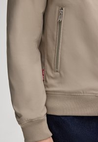 Beżowa, lekka kurtka z zamkiem błyskawicznym, z kieszenią na zamek, ściągaczami na mankietach i elastycznym pasem. Teksturowana tkanina o gładkim wykończeniu.