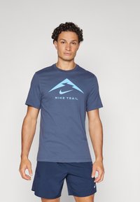 Tumesinine lühikeste varrukatega T-särk, millel on helesinine graafika mäest ja tekst "NIKE TRAIL" keskel all. Pehme kangas, ümmargune kaelus.