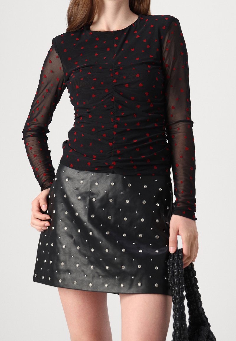 Svart långärmad topp med röda hjärtmönster och rynkade detaljer, kombinerad med en svart läderkjol med silvernitar. Svart flätad väska.