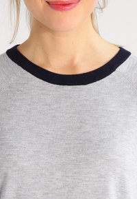 Sudadera gris con cuello acanalado azul marino, que presenta una textura suave y un diseño sencillo. El cuello es de estilo redondo, adecuado para uso casual.