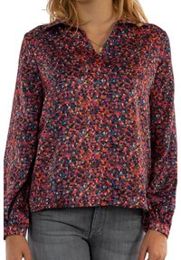 Long-sleeve blouse in patterned fabric featuring vibrant colors like red, pink, blue, and black. V-neck design with a loose fit.