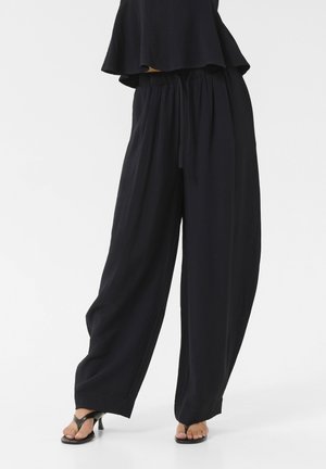 Black, loosely fitted pants with a high waist and elastic band, featuring a soft, textured fabric. The design includes wide legs and side seams.