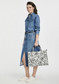 Sukienka koszulowa z denimu z przednimi guzikami i bocznym rozcięciem, w połączeniu z torbą w kwiatowy wzór i białymi sneakerami. Posiada dopasowany pas.