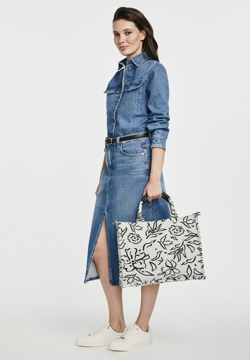 Sukienka koszulowa z denimu z przednimi guzikami i bocznym rozcięciem, w połączeniu z torbą w kwiatowy wzór i białymi sneakerami. Posiada dopasowany pas.