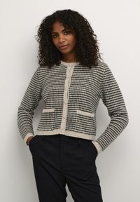 Knitted cardigan in dark green and cream with a textured polka dot pattern, round neckline, button front, and two front pockets.