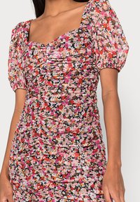 Robe mini fleurie avec décolleté carré, manches bouffantes et détails froncés. Les couleurs comprennent des motifs floraux en rose, noir, orange et blanc.
