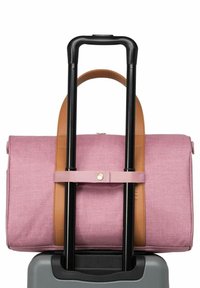 Sac en tissu rose avec des accents en cuir marron fixé à une poignée de valise noire. Présente une texture lisse et un détail de bouton sur la sangle.