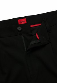 Pantalones negros con cierre de botón y cremallera. La parte interior de la cinturilla incluye un acento rojo en contraste. Fabricados con tela texturizada.