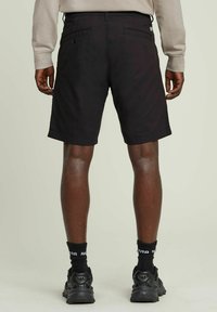 Shorts neri in cotone con due tasche posteriori e taglio dritto. Abbinati a sneakers nere e calze coordinate, visti da dietro.