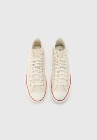 Hochschäfte Sneaker aus off-weißen Canvas mit roten Akzenten, weißen Schnürsenkeln, gummierter Zehenkappe und strukturiertem Boden, von oben präsentiert.