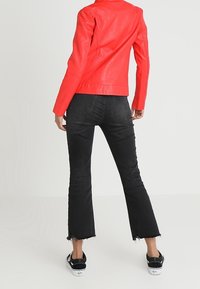 Veste en cuir rouge au design ajusté, associée à un jean noir évasé avec des ourlets effilochés et des chaussures noires à semelles blanches.