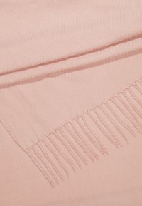 Tissu tissé rose pâle doux avec une rangée de glands torsadés uniformément espacés le long d'un bord.